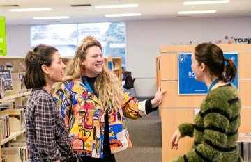 three women (staff) talking inside library