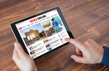 close up of hands scrolling on a tablet device. Displays a newspaper page on screen.